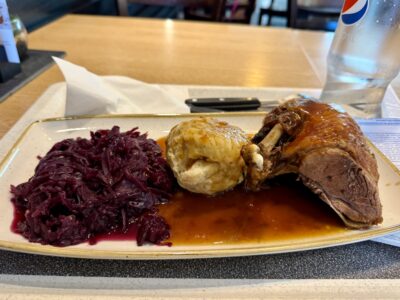 Ein länglicher Teller auf einem Tablett, von links nach rechts: Blaukraut, Semmelknödel, Teil einer Ente